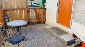 A patio area with a round table and two chairs, a wooden fence, and an orange door.