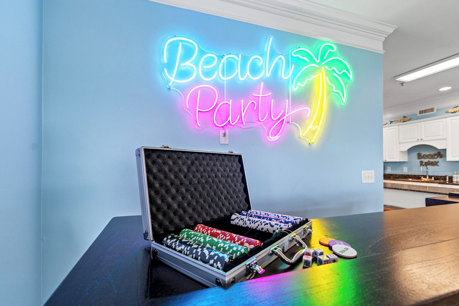 Un letrero de neón que dice "Beach Party", con una palmera, una mesa de póker con fichas y dados.