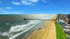 Ein Strand mit einem Steg, der sich ins Meer erstreckt, neben einer Küstenstadt mit Gebäuden und blauem Himmel.