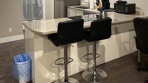 A modern kitchen with a central island, bar stools, a refrigerator, a microwave, and a coffee maker. - Cozy Downtown Studio (Moncton)