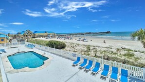 A pool area with lounge chairs, a pier extending into the ocean, and a beach in the background.
