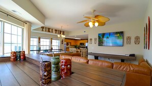 A spacious living area with a pool table, leather seating, and tiki-themed decor.