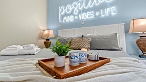 A neatly arranged bedroom with a bed, pillows, a bedside lamp, a tray with decorative items, and a wall sign that reads "positive mind vibes life". - Seas The Day-POOL/Spa/GAME ROOM/Views/BIKES/Steps to beach (North Myrtle Beach)