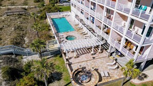 An aerial view of a hotel with a swimming pool, outdoor seating, and a hot tub. - Seas The Day-POOL/Spa/GAME ROOM/Views/BIKES/Steps to beach (North Myrtle Beach)