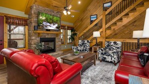 A spacious living room with a stone fireplace, red leather sofas, a wooden coffee table, and a TV mounted on the wall. - Time for Us (Gatlinburg)