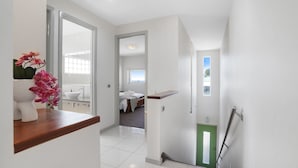 Passadís modern d'hotel amb un taulell de fusta, una porta verda i vista a un dormitori amb un llit i una finestra.