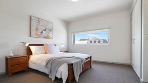 Ein Schlafzimmer mit Bett, Nachttischen, einem Fenster und einem Bild an der Wand.