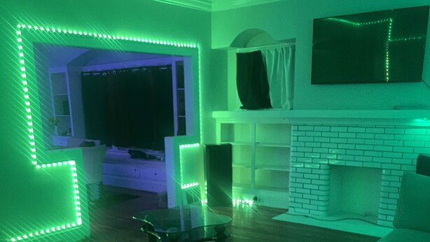 Ein Wohnzimmer mit grüner LED-Beleuchtung, einem Kamin und einem darüber montierten Fernseher.