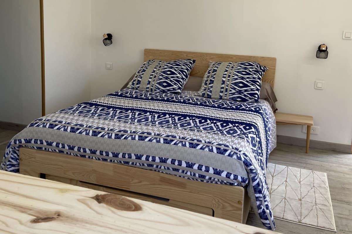 A bedroom with a wooden bed, patterned bedding, a bedside table, and a nightstand.