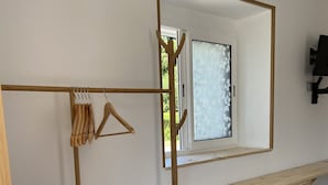 A room with a wooden dresser, a wooden coat rack, and a mirror. - A la fontaine fleurie (Fremifontaine)