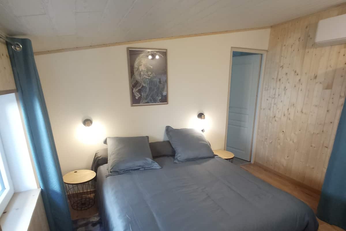 A bedroom with a large bed, two bedside tables, a window with curtains, and a wooden wall panel.