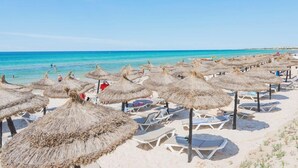 A beach with thatched umbrellas and sun loungers.