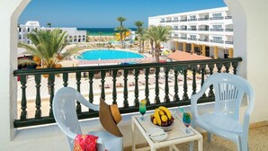 A balcony with a view of a swimming pool, palm trees, and a hotel building.