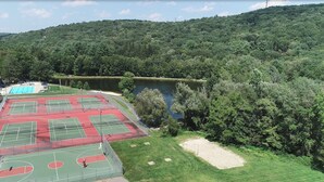 Een tenniscomplex met meerdere banen, omringd door weelderige begroeiing en een meer.