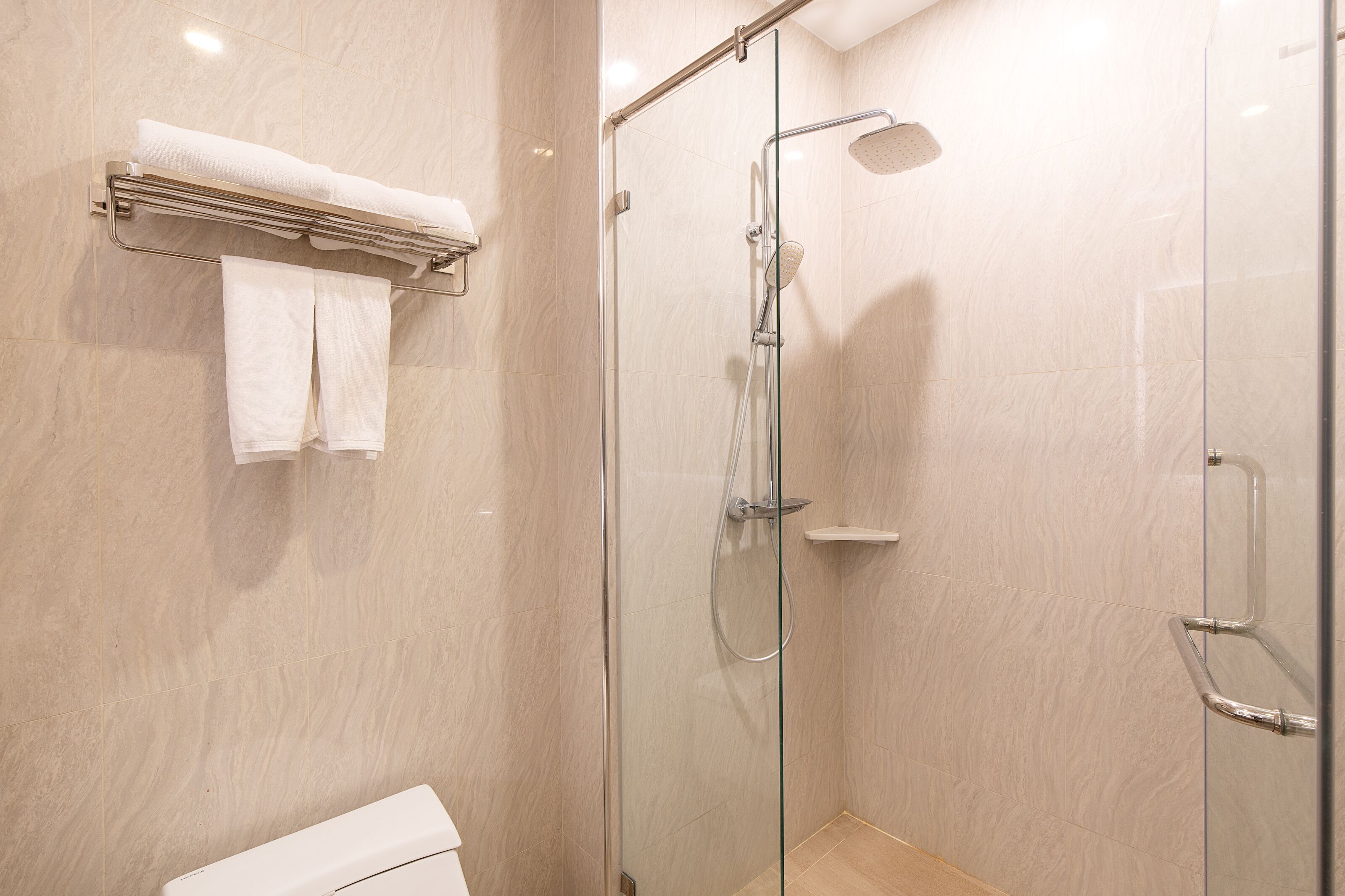 Un baño moderno con ducha acristalada, inodoro y toallero con toallas dobladas.