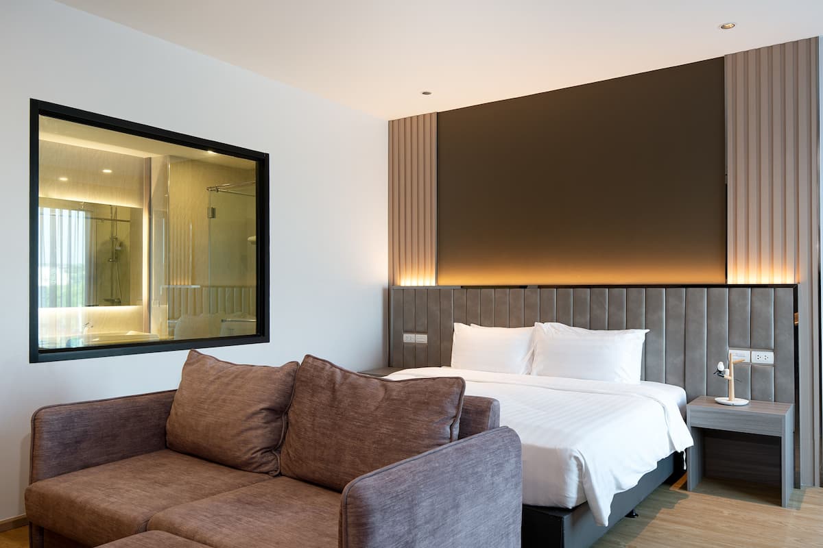 Una habitación de hotel moderna con una cama grande, un sofá, un espejo y una mesita de noche con una lámpara.