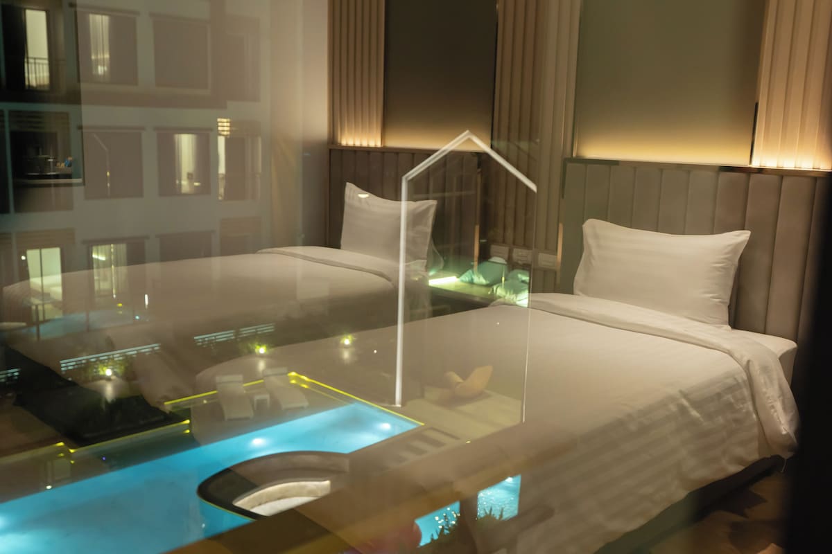 Una habitación de hotel moderna con una cama de cristal, vistas a la ciudad y un amplio ventanal con cortinas.
