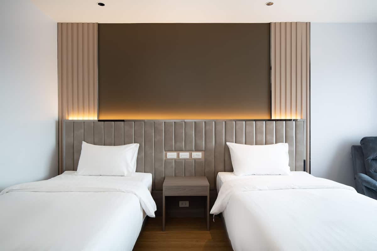 Habitación de hotel con dos camas, cabecero de madera y una mesita de noche con toma de corriente.