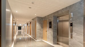 Un pasillo moderno con piso de mármol, puertas de madera y un ascensor.