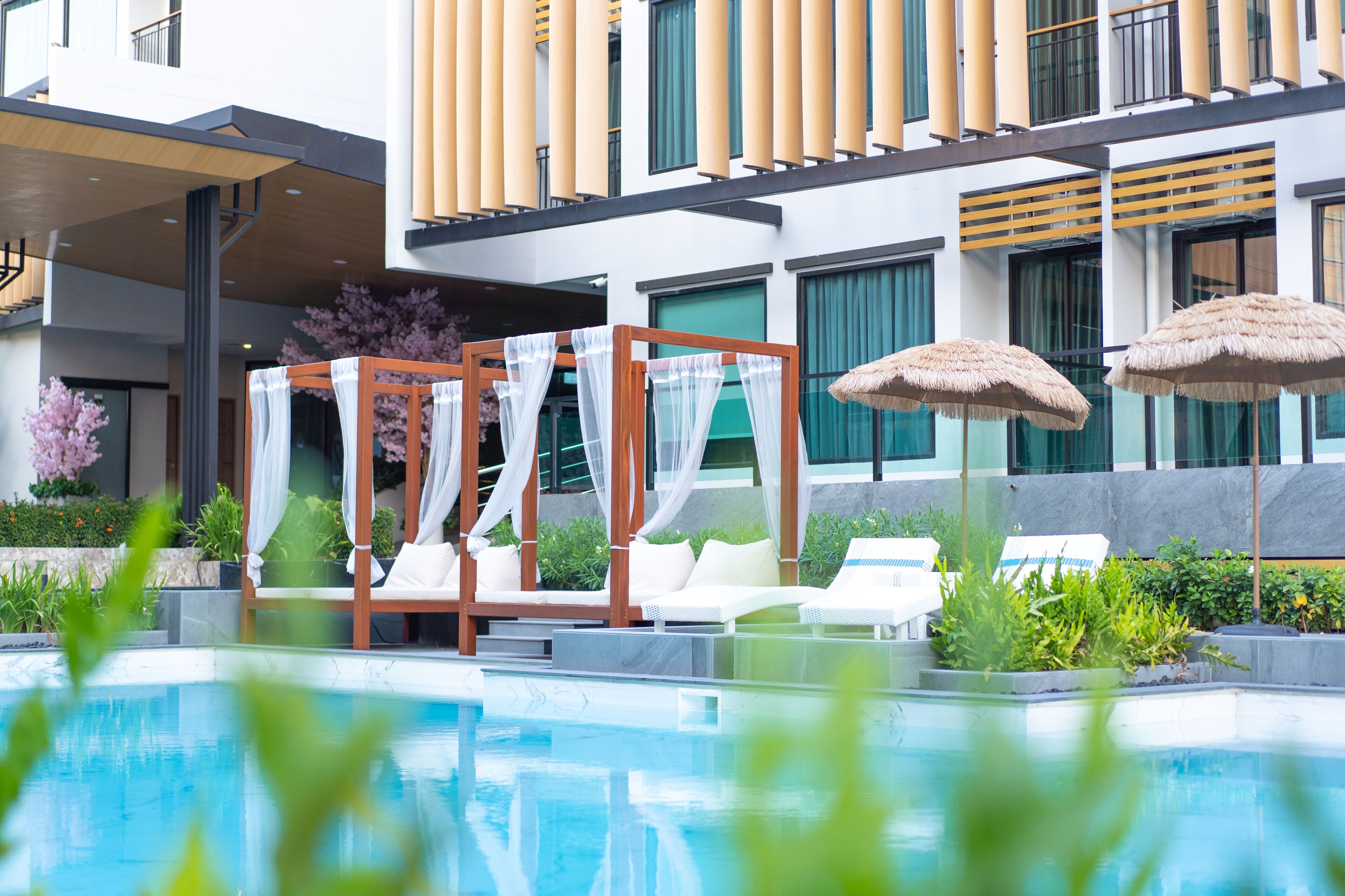 A modern hotel with a pool area, including a cabana, lounge chairs, and umbrellas.