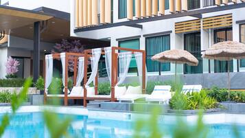 A modern hotel with a pool area, including a cabana, lounge chairs, and umbrellas.