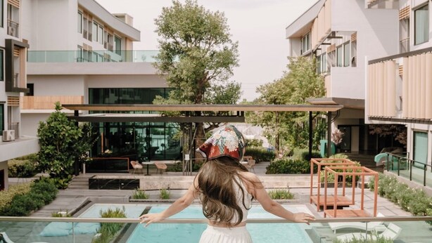 Una mujer con vestido blanco parada al borde de una piscina en la azotea, con vista a edificios modernos y un cielo despejado.
