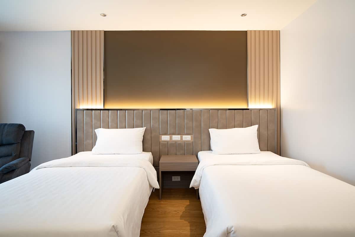 Habitación de hotel con dos camas, una mesita de noche, una silla y un televisor grande montado en la pared.