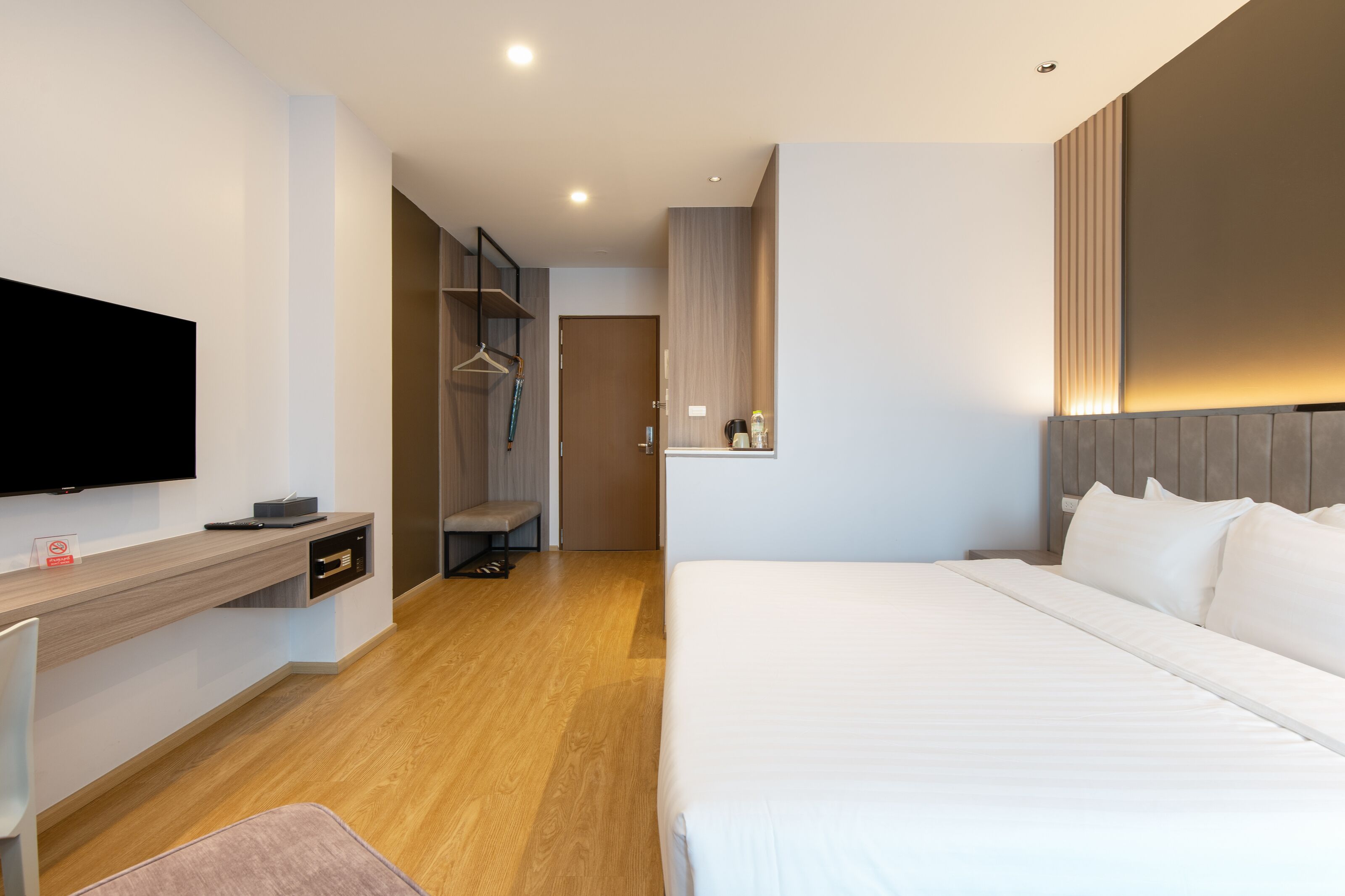 A modern hotel room with a bed, a desk, a TV, and a wardrobe.