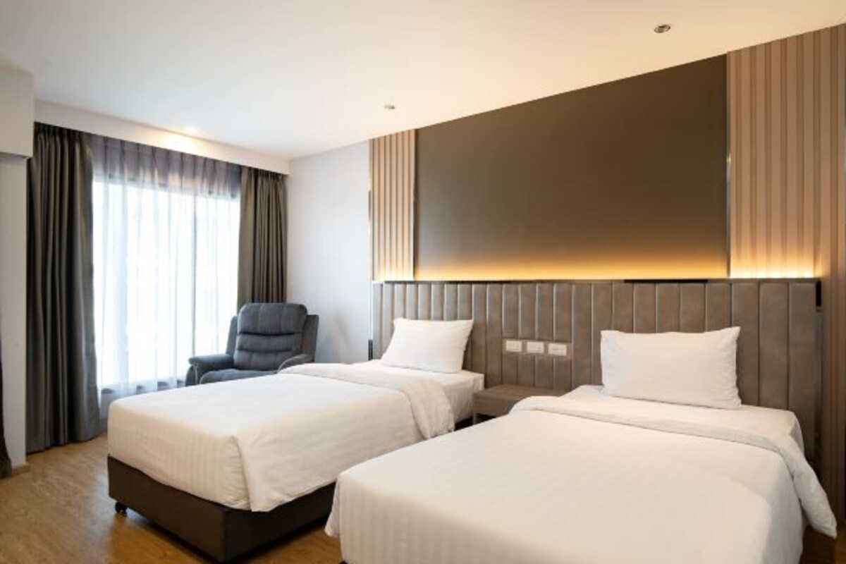 Habitación de hotel con dos camas, una silla y un televisor grande montado en la pared.