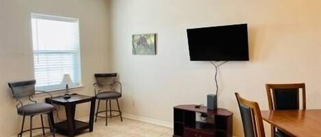 A dining area with a TV mounted on the wall, a small table with chairs, and a cabinet.