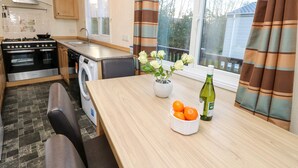 A compact kitchen with a stove, oven, washing machine, and a dining area with a table, chairs, and a vase with flowers. - The Goodwood Annex (Chichester)