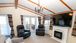 A living room with a sofa, two leather recliners, a fireplace, a TV, and a balcony with curtains. - The Goodwood Annex (Chichester)
