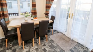 A dining area with a wooden table, four chairs, a vase with flowers, a bottle of wine, and a bowl of oranges. - The Goodwood Annex (Chichester)