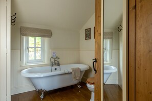 Ein Badezimmer mit einer Badewanne auf Füßen, einem weißen Waschbecken und einer Holztür.
