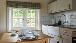 Una cocina con una mesa de comedor dispuesta para el té, armarios blancos y una ventana con vista a la vegetación.
