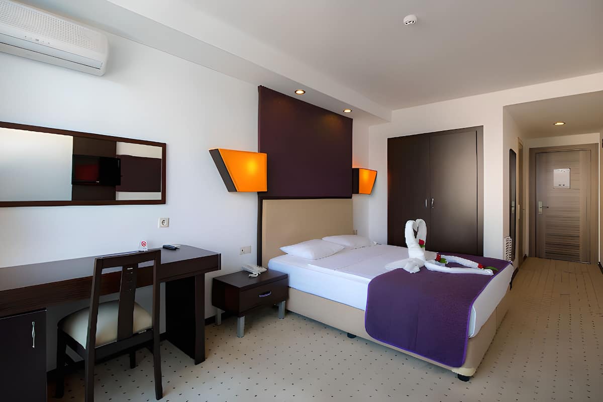 A hotel room with a bed, desk, chair, and a mirror.