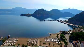 A coastal area with a beach, a marina, and mountains in the background.