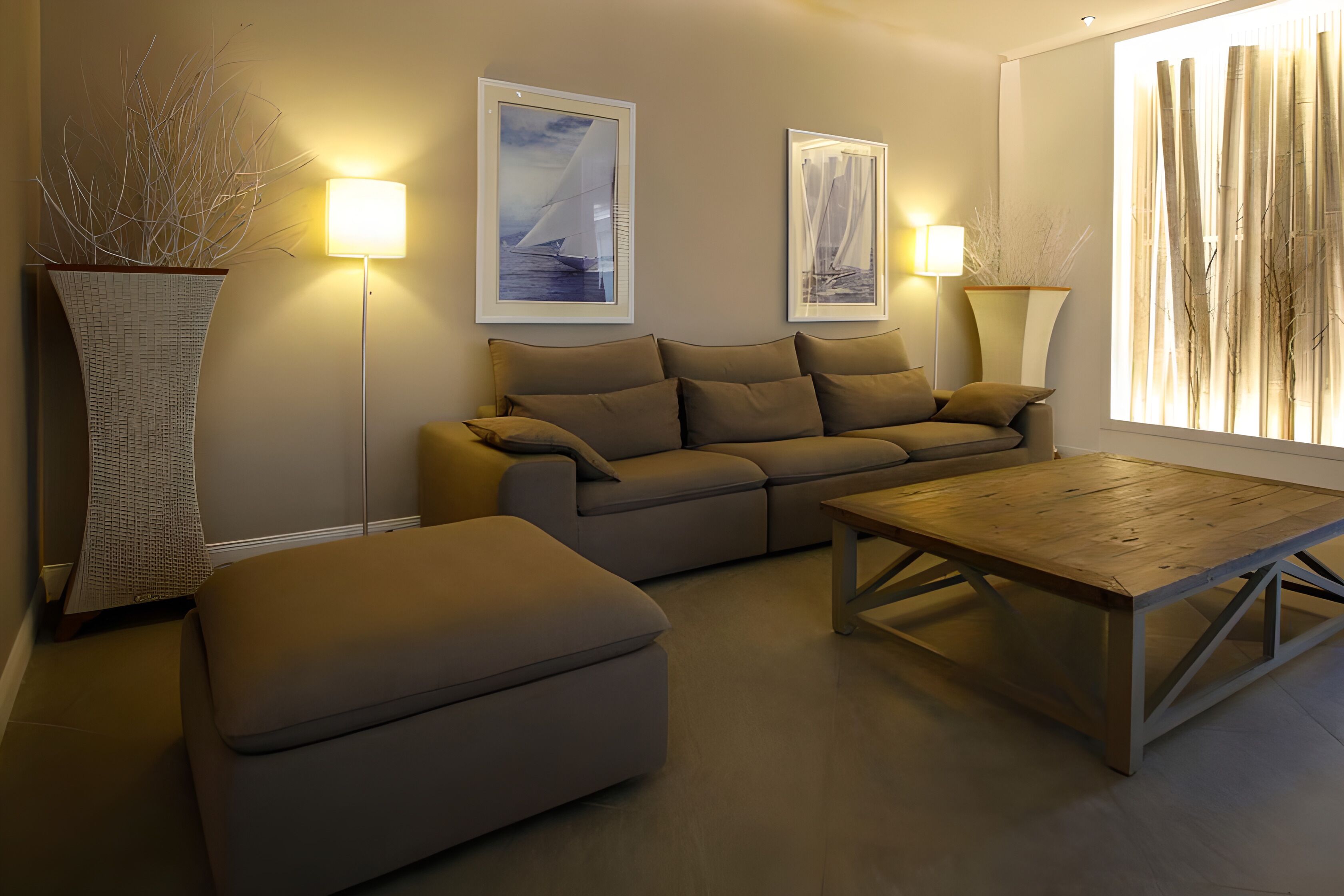 Una sala de estar moderna con sofá, reposapiés y mesa de centro, una obra de arte enmarcada en la pared y una lámpara de pie.