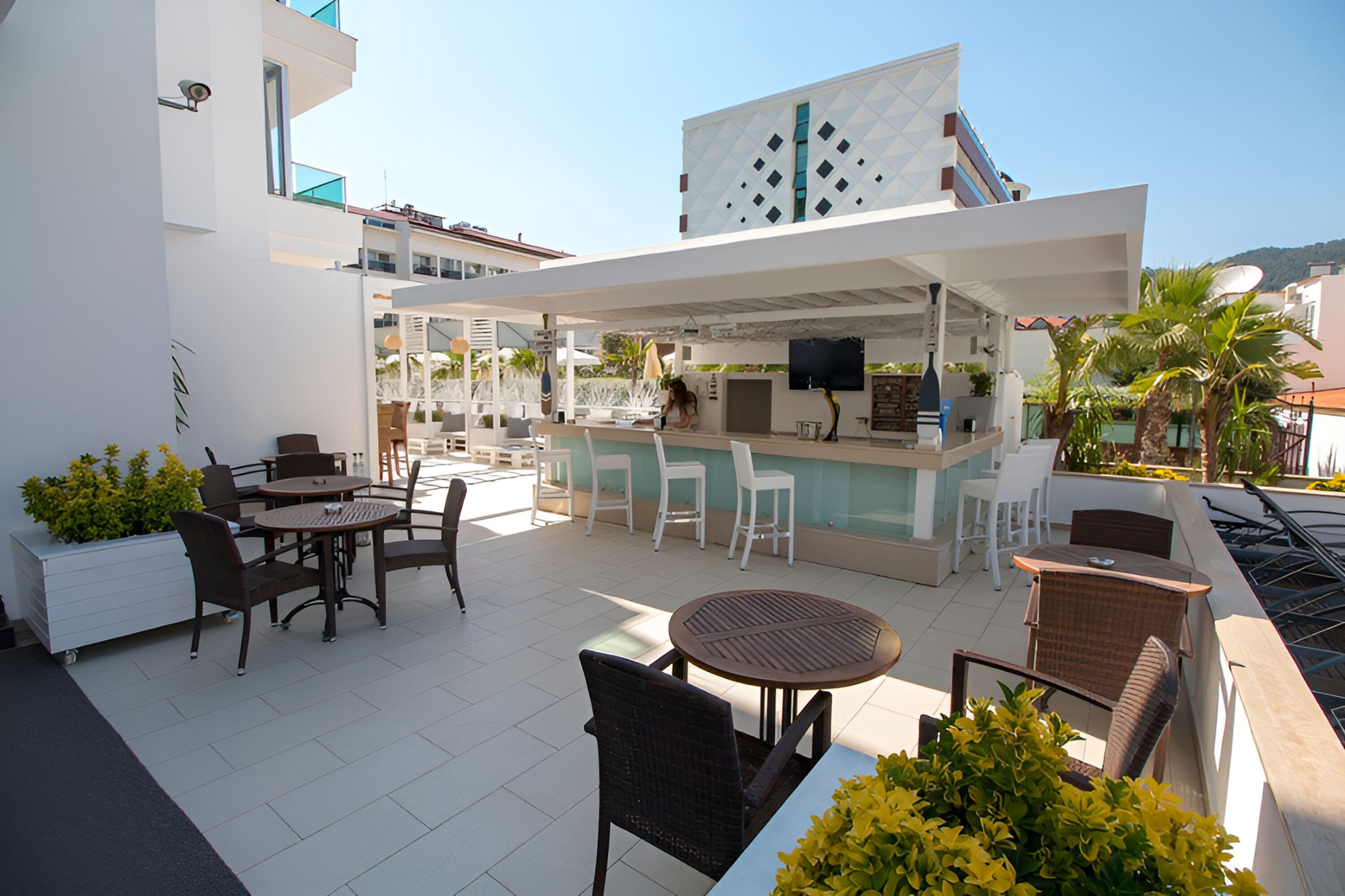 Uma área de estar ao ar livre com mesas e cadeiras redondas, um bar e uma piscina.