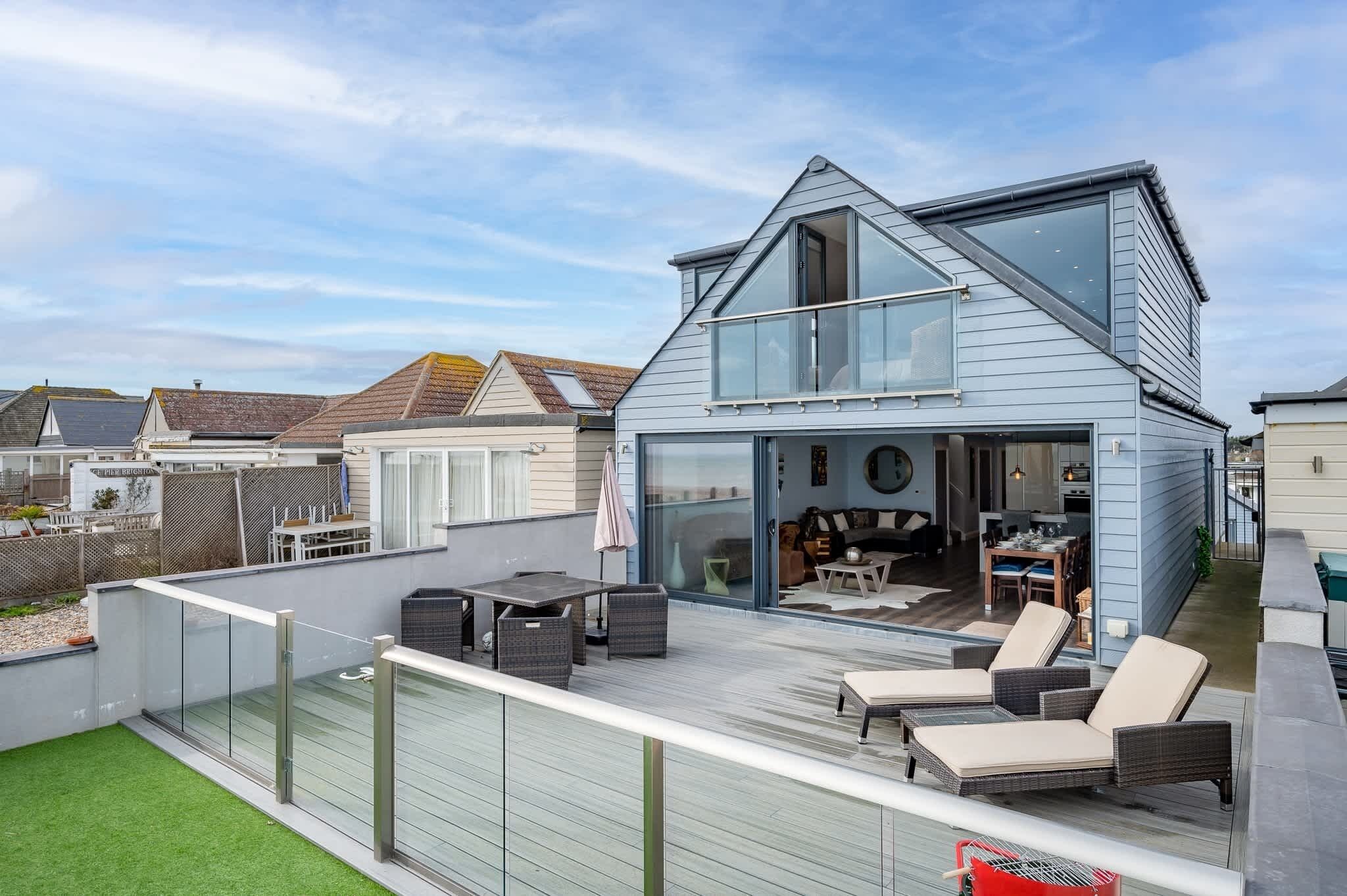 A modern two-story house with a balcony, outdoor seating, and a visible kitchen area.