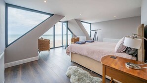 A bedroom with a large window, a bed, a chair, and a desk.