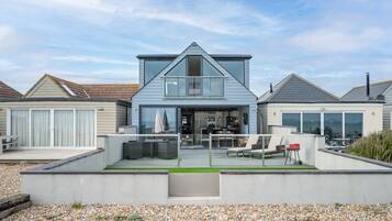 A modern two-story house with a flat roof, large windows, and a patio area with outdoor furniture.