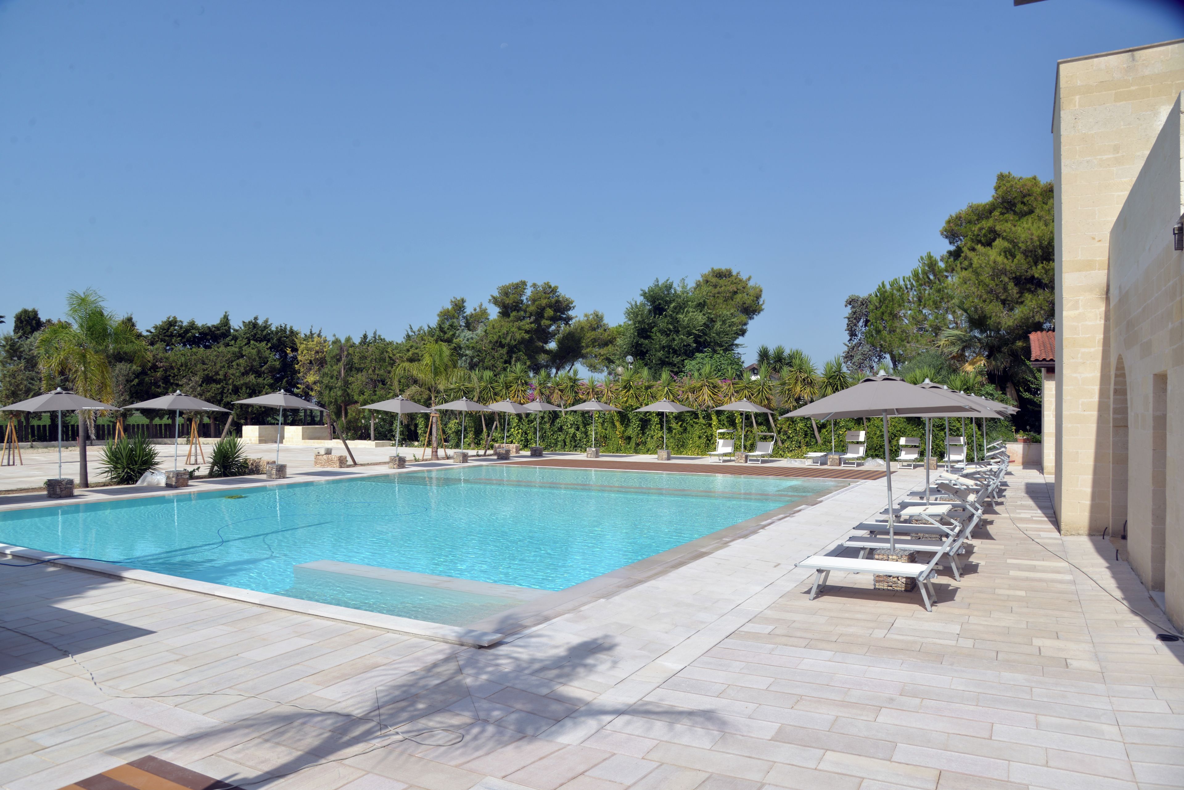 A swimming pool with lounge chairs and umbrellas, surrounded by trees and a building.