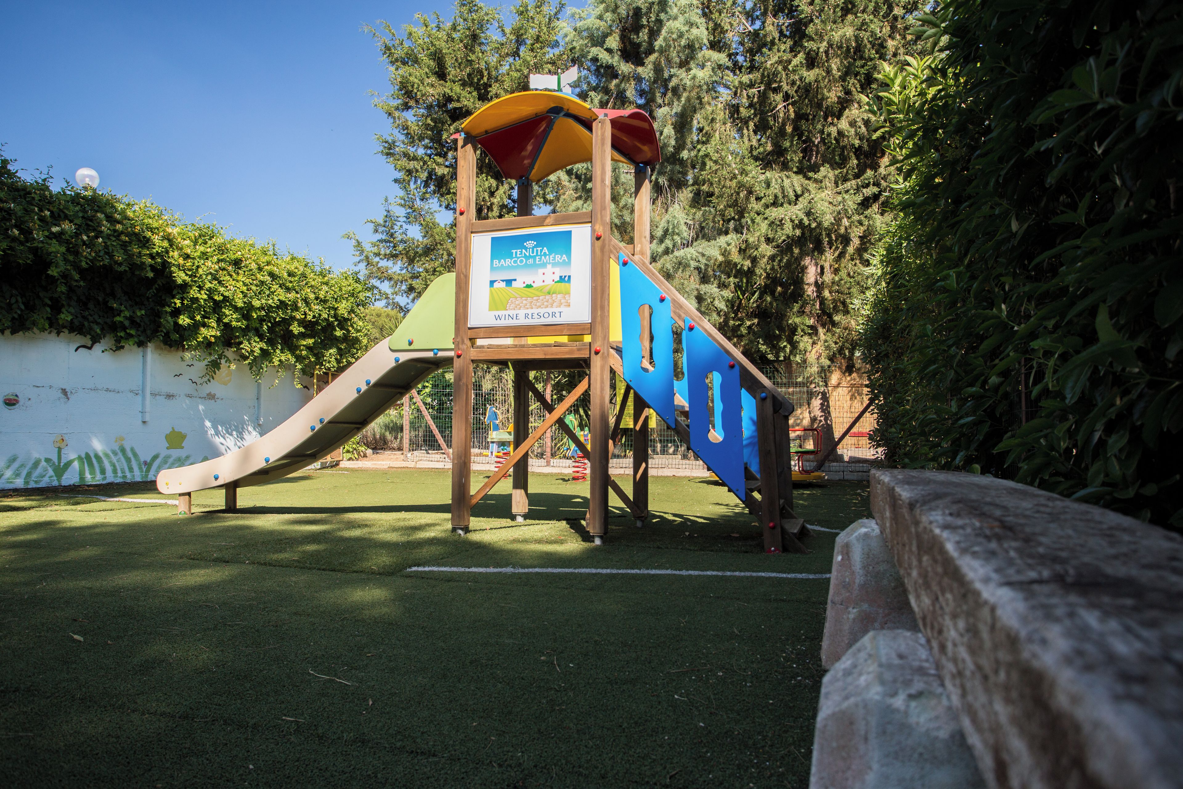 A playground with a slide and climbing structure, surrounded by greenery.