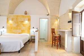 A hotel room with a bed, a chair, a small table, and a stone wall. - Tenuta del Barco (Taranto)