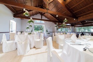 A spacious hall with high wooden ceilings and large windows, furnished with white tables and chairs, and decorated with hanging plants. - Tenuta del Barco (Taranto)