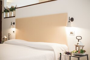A neatly made bed with a white bedspread, a bedside table with a lamp, a small plant, and a decorative item. - Tenuta del Barco (Taranto)