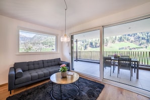 A modern living room with a sofa, a coffee table, and a view of a balcony with outdoor furniture.