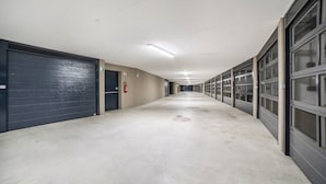 A long, narrow hallway with a series of closed doors on the left, a fire extinguisher on the wall, and a fire exit sign. - Apartment 'Sankt Martin' with Mountain View, Private Terrace and Wi-Fi (Sankt Martin)