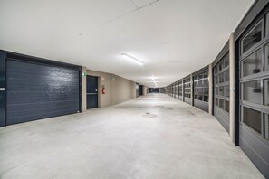 Un long couloir étroit, avec une série de portes fermées sur le côté gauche, un extincteur accroché au mur et un panneau indiquant la sortie de secours.